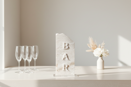 Decorative 'BAR' sign with wine glasses and a vase on a shelf.