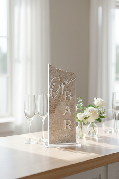 Decorative 'Open Bar' sign on a table with glasses and flowers in a bright room.