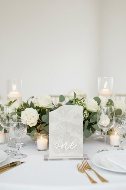 Elegant table setting with white flowers, candles, and a marble 'one' sign.