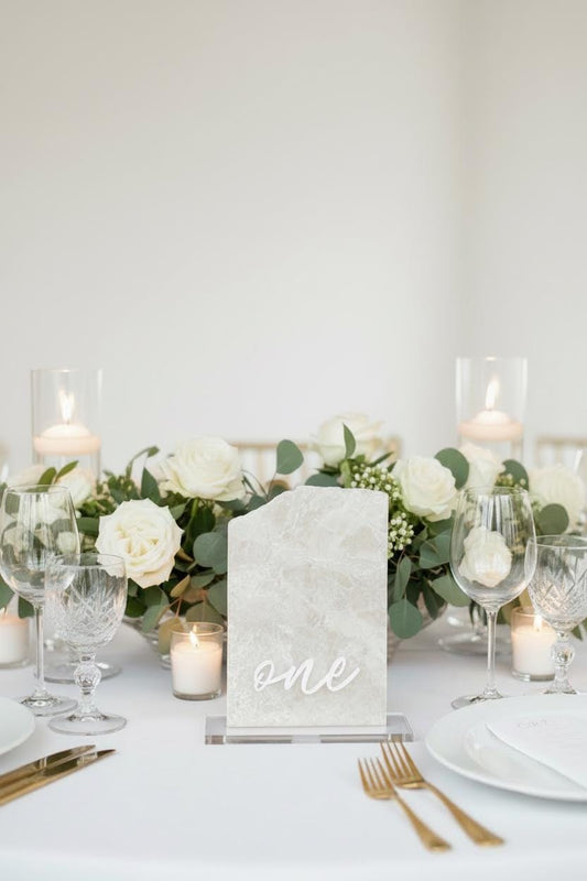 Elegant table setting with white flowers, candles, and a marble 'one' sign.
